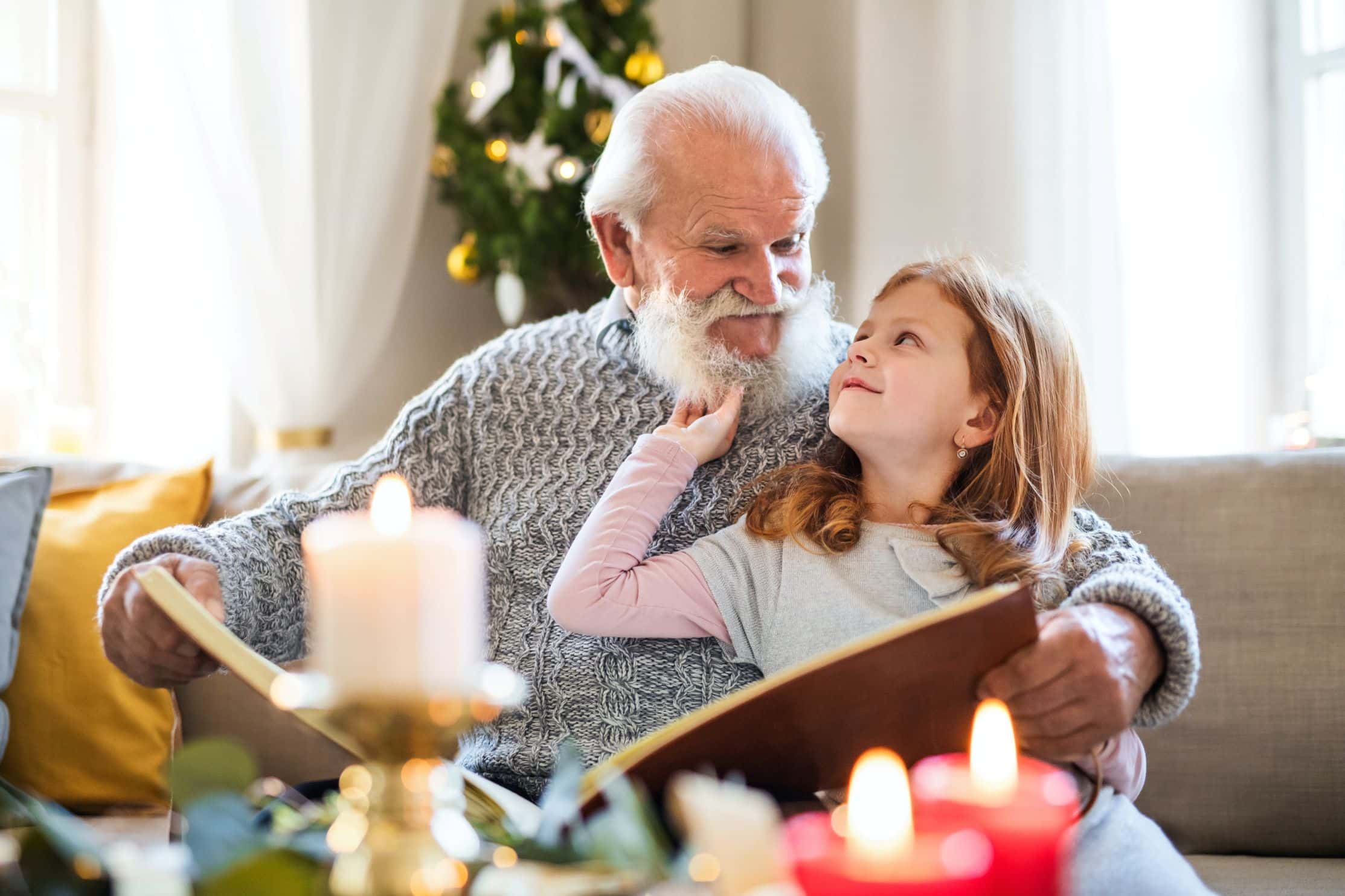 Grandpa and Granddaughter reading together on the couch at Christmas for a blog post teaching people how to know if their elderly parents need help. 