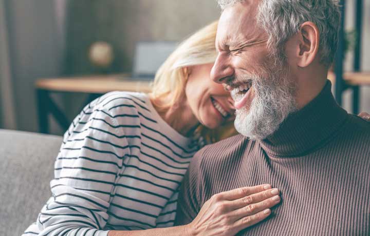 Older couple laughing on a couch.